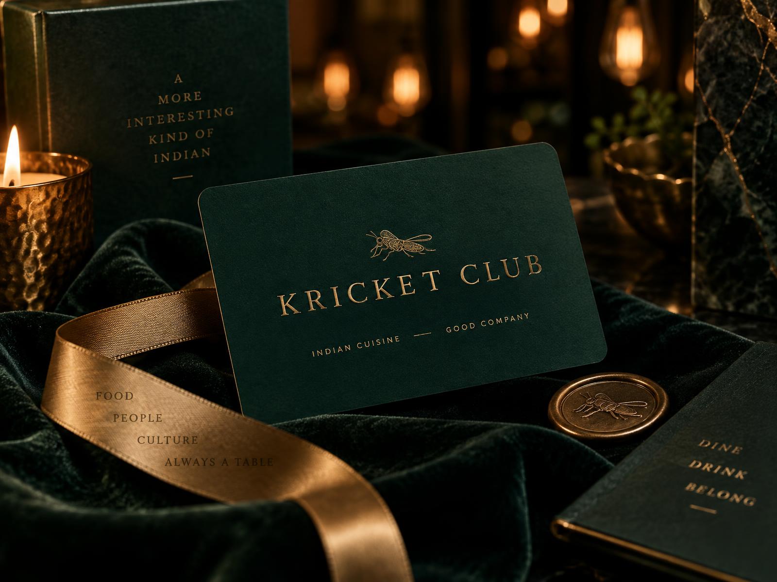A Kricket Club gift card in deep emerald with brass lettering, resting on velvet beside a candle